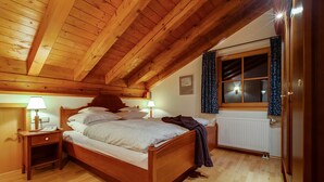 A wooden-framed bedroom with a bed, bedside lamps, a window with curtains, and a radiator.