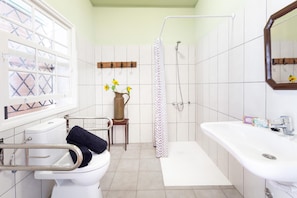 Casa de banho com sanita, lavatório, chuveiro e janela com padrão decorativo.