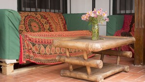 Una habitación con un sofá verde cubierto con un edredón estampado, una mesa de madera con un jarrón de flores y un piso de baldosas.