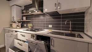 A modern kitchen with a built-in dishwasher, stainless steel appliances, and black tiled backsplash.