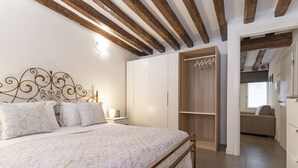 A bedroom with a bed, wooden beams, a wardrobe, and a bathroom visible through an open door.