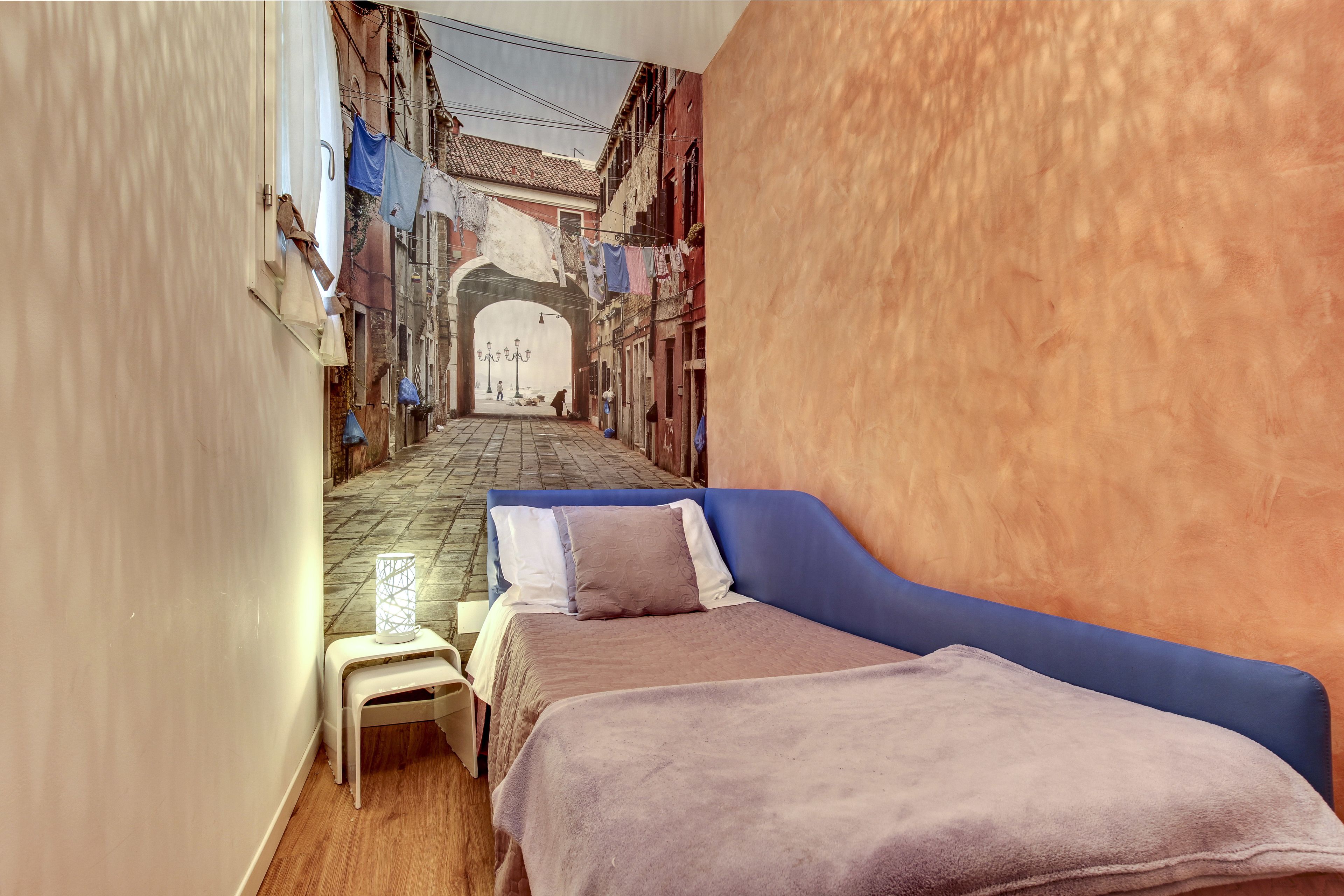 Un estrecho callejón que conduce a una puerta, con una cama y una pequeña mesa en primer plano.