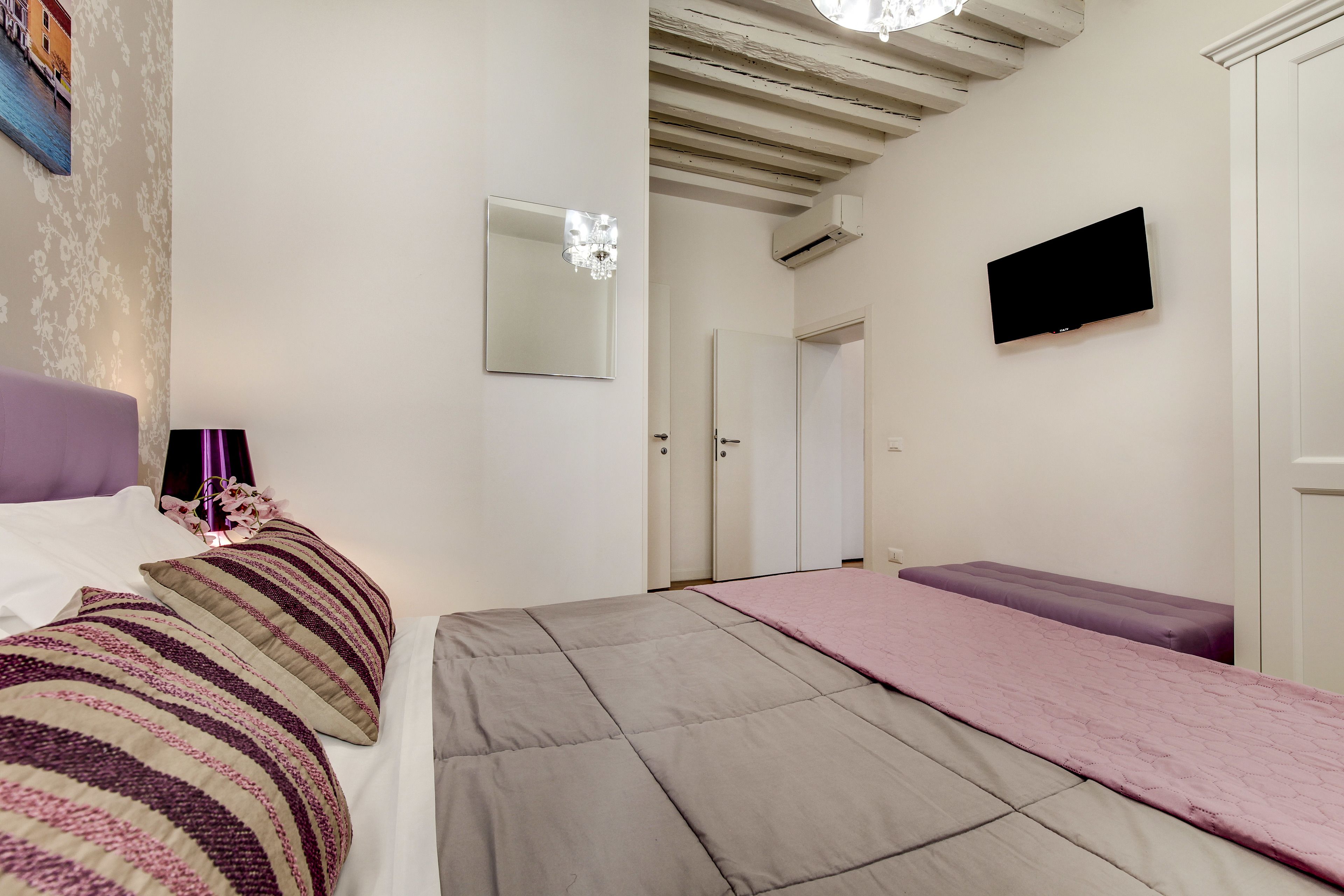 A bedroom with a bed, a bench, a TV, and a door.