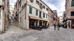 A narrow street with outdoor seating at a cafe, surrounded by historic buildings with shutters and balconies. - Charming Castello Apartments by Wonderful Italy (Venice)