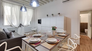 A dining area with a table set for four, white chairs, a sofa, and a cabinet with decorative items. - Charming Castello Apartments by Wonderful Italy (Venice)