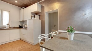 A modern kitchen with white cabinets, a built-in microwave, and a dining area with a table and chairs. - Charming Castello Apartments by Wonderful Italy (Venice)