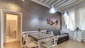 A modern living room with a dining table, white chairs, a grey sofa, and a large window with sheer curtains. - Charming Castello Apartments by Wonderful Italy (Venice)