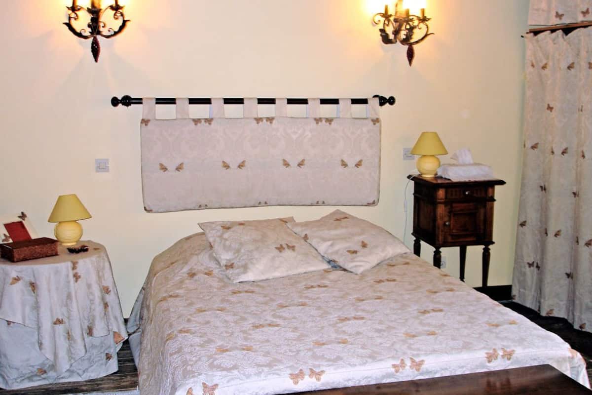 A bedroom with a bed, two bedside tables with lamps, a nightstand, and a wall-mounted lamp.