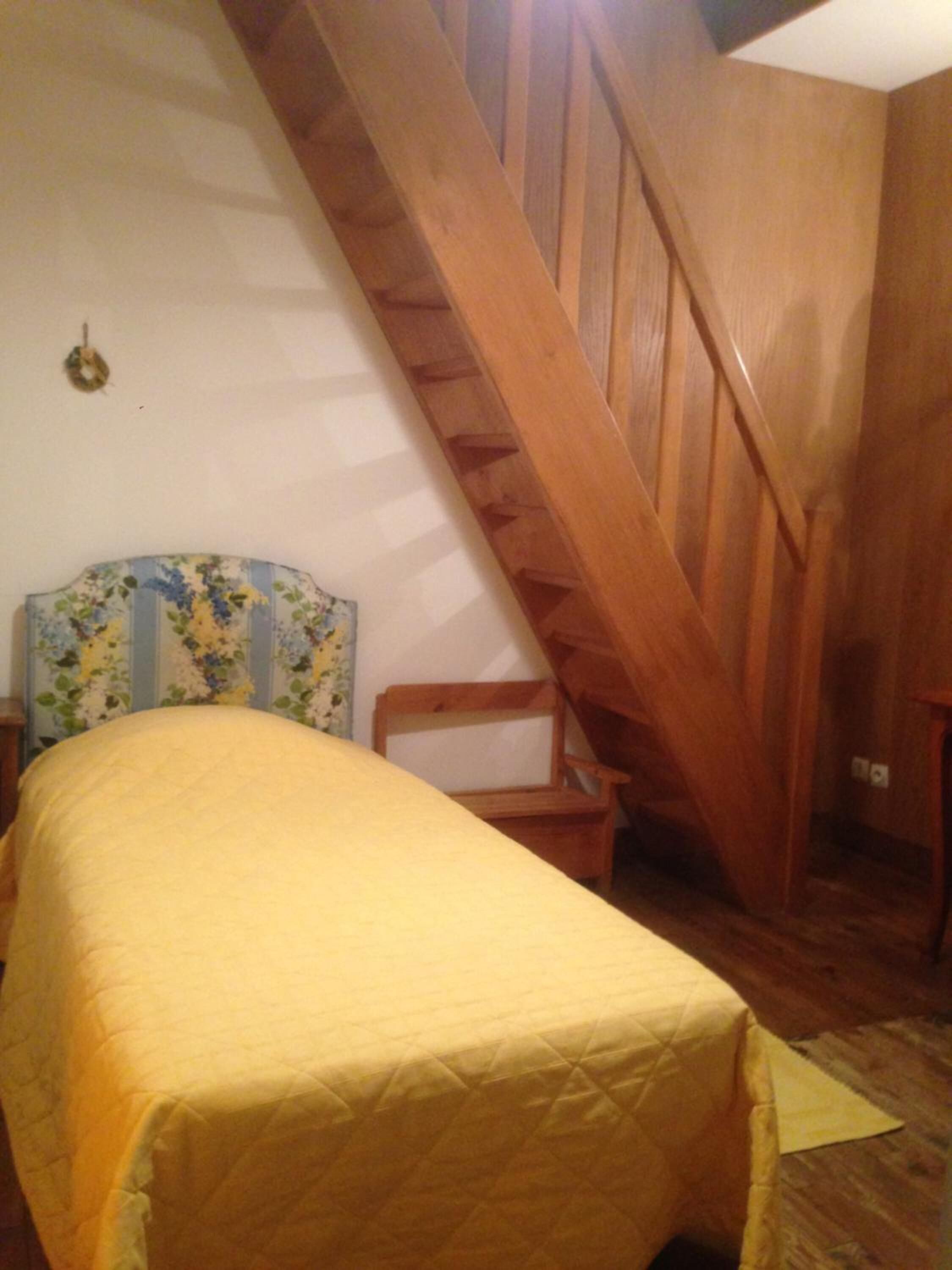 A bedroom with a bed, a wooden staircase, and a headboard with floral patterns.