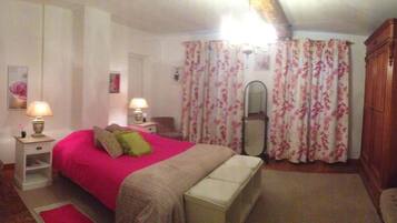 A bedroom with a bed, bedside tables, a chair, a wardrobe, and floral curtains.