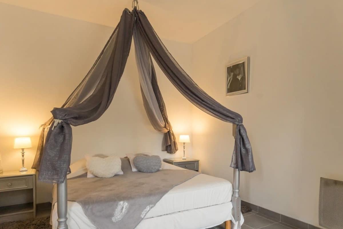 A bedroom with a canopy bed, two bedside tables with lamps, a framed picture on the wall, and a radiator.