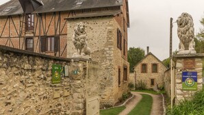 A traditional stone building with a lion statue on the entrance, a sign indicating 'Gîte 8', and a smaller building in the background. - Le Moulin de la Côte - Chambre d'Hôtes (Saint-Vigor)