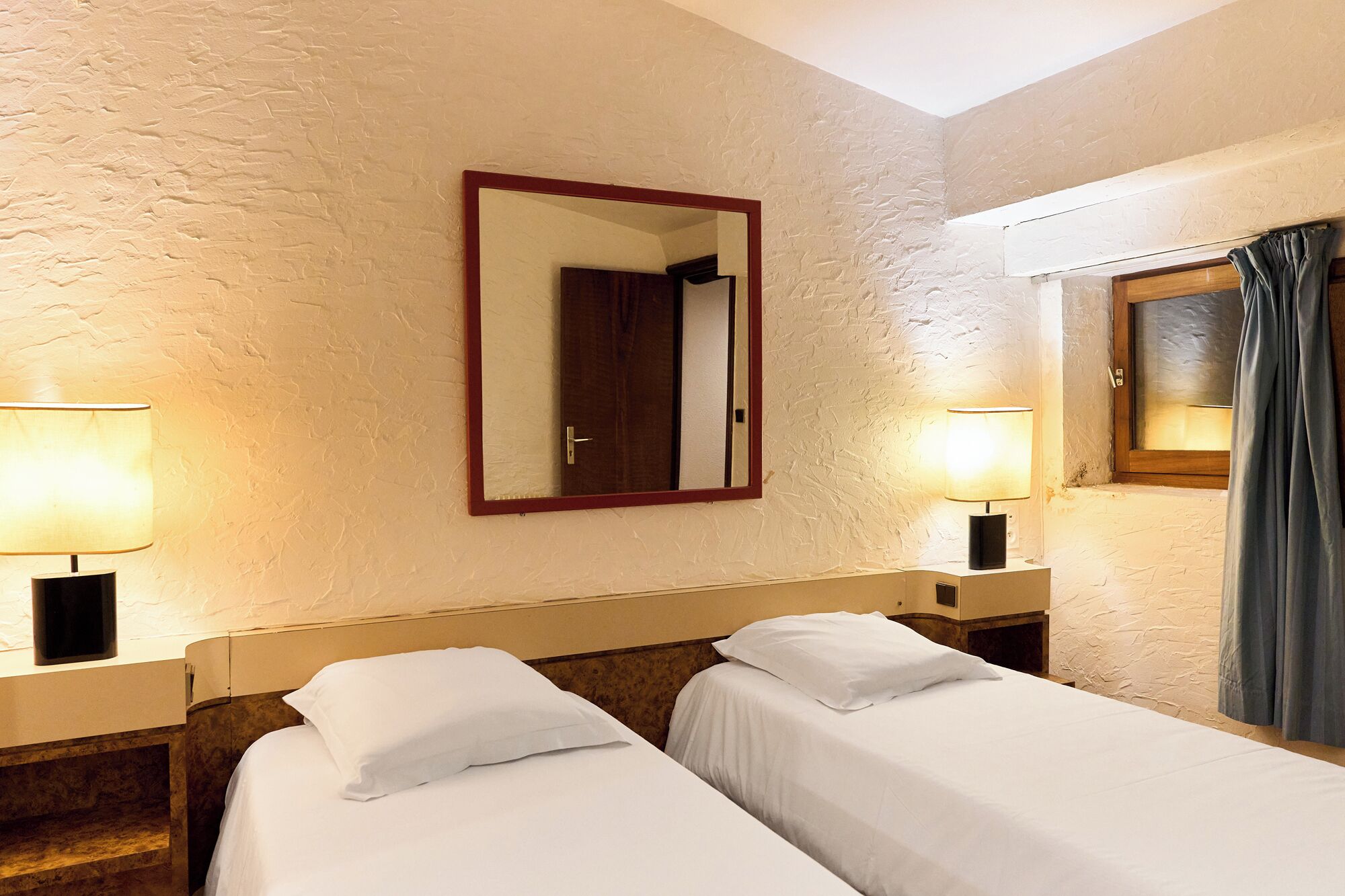 Une chambre d’hôtel avec deux lits simples, un grand miroir et deux lampes de chevet.