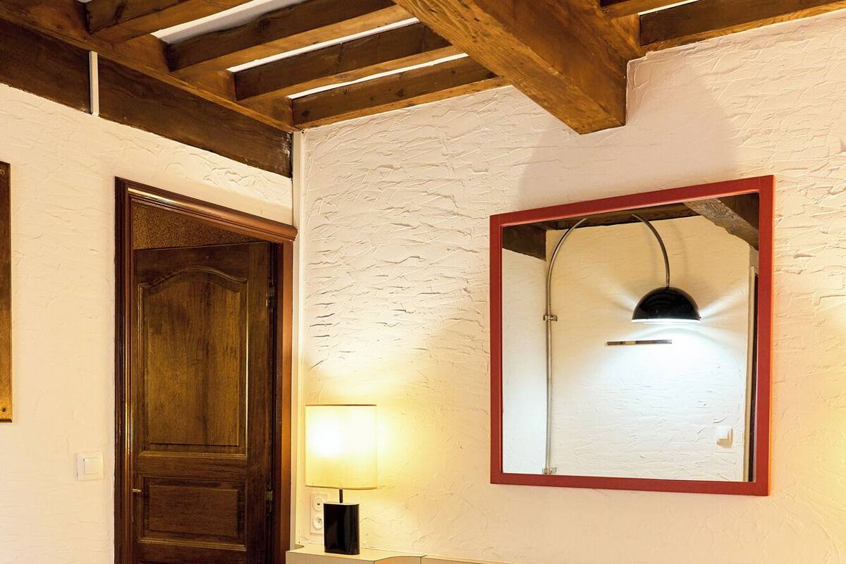 A single bed with white linens in a room with exposed wooden beams and a white textured wall.