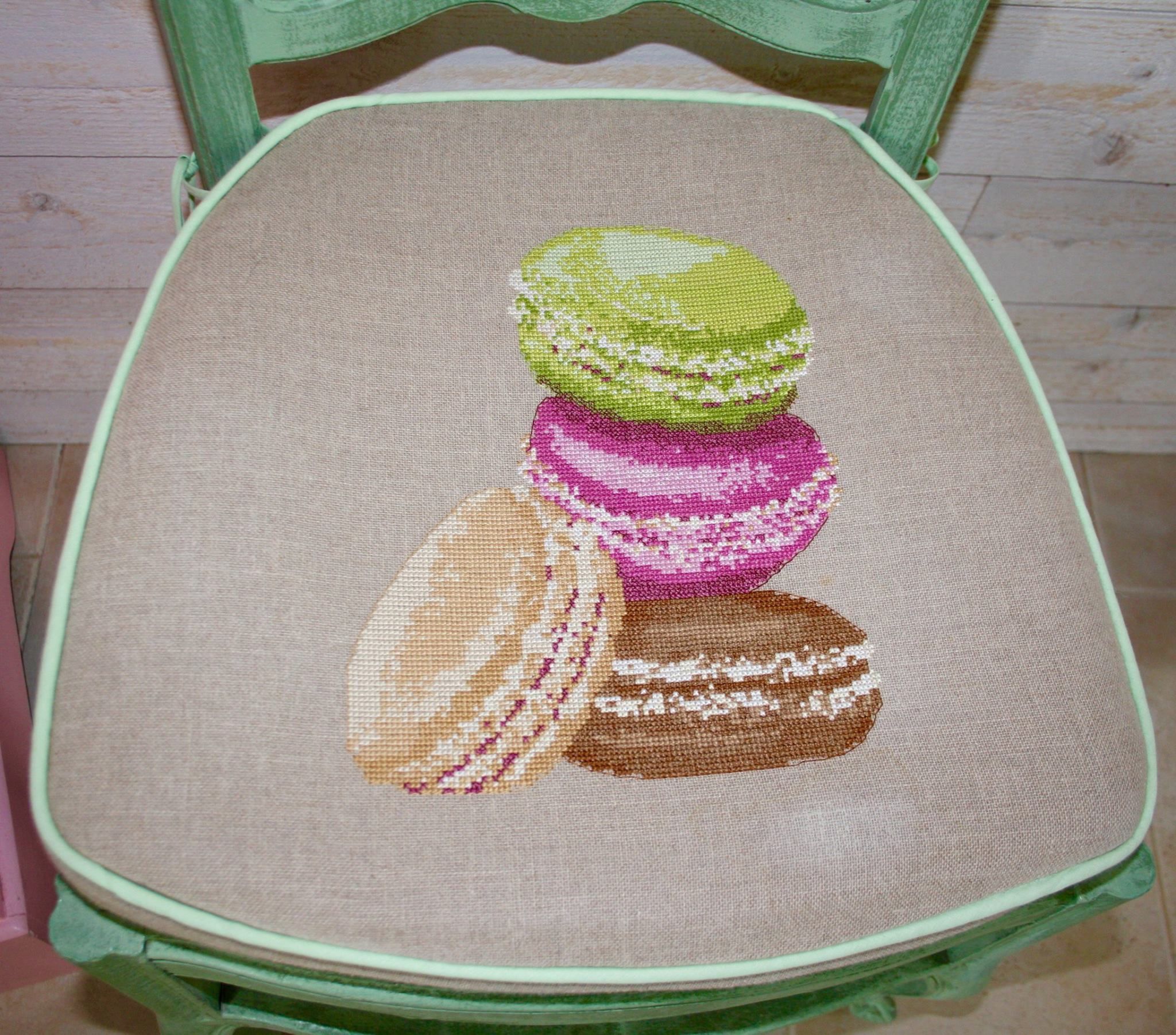 A chair with a cushion featuring a cross-stitch design of macarons.