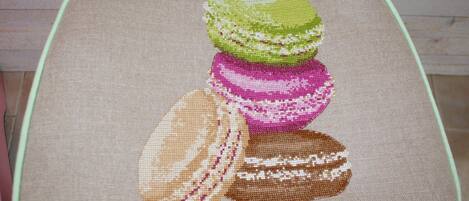 A chair with a cushion featuring a cross-stitch design of macarons.