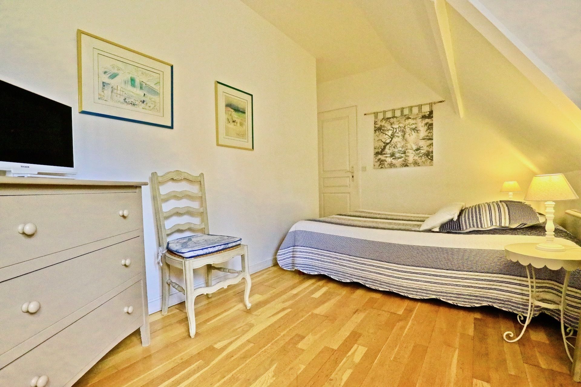 A bedroom with a bed, a chair, a dresser, a TV, and framed pictures on the wall.