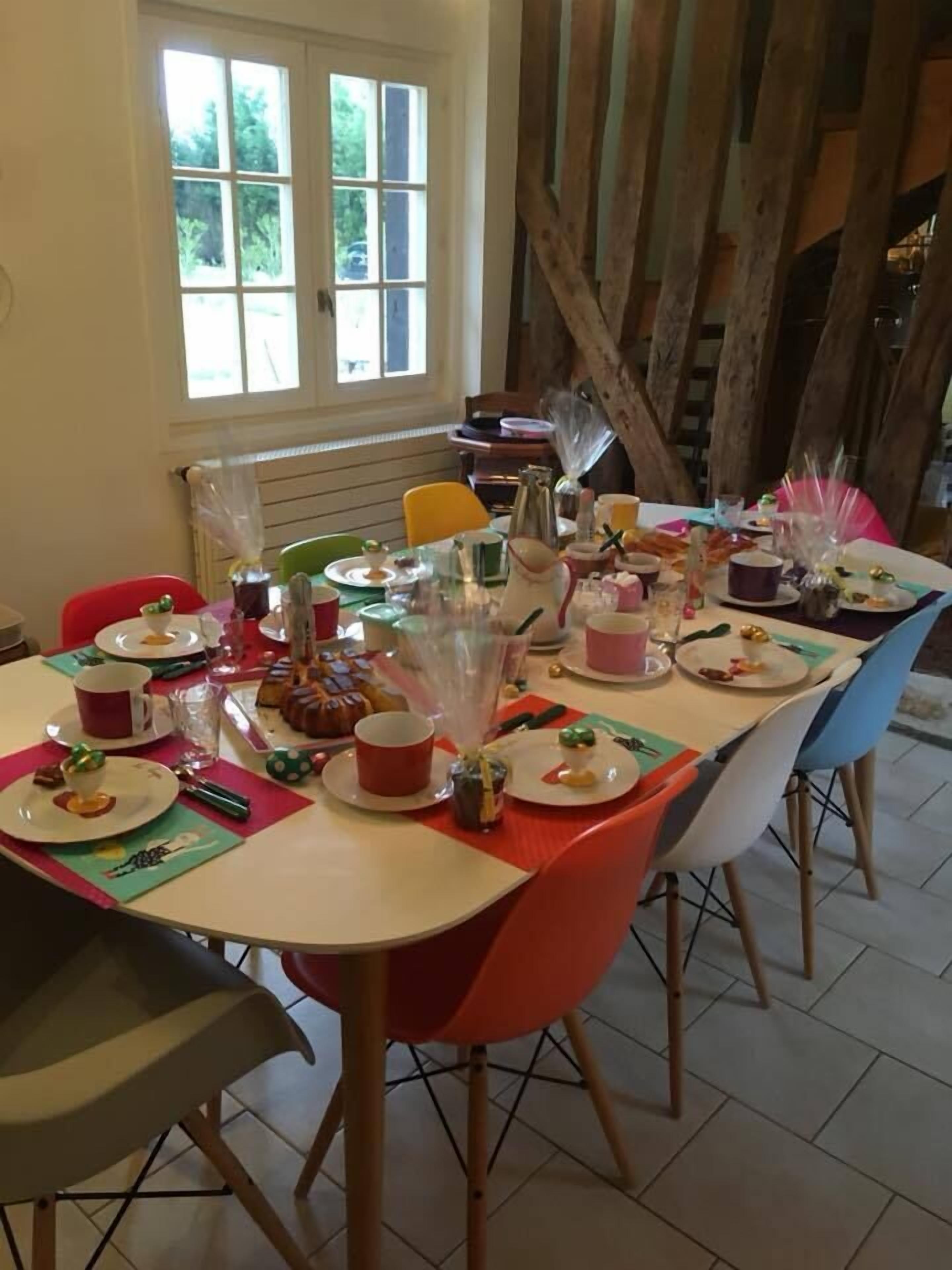Una mesa de comedor dispuesta con platos, vasos y diferentes alimentos, rodeada de sillas.