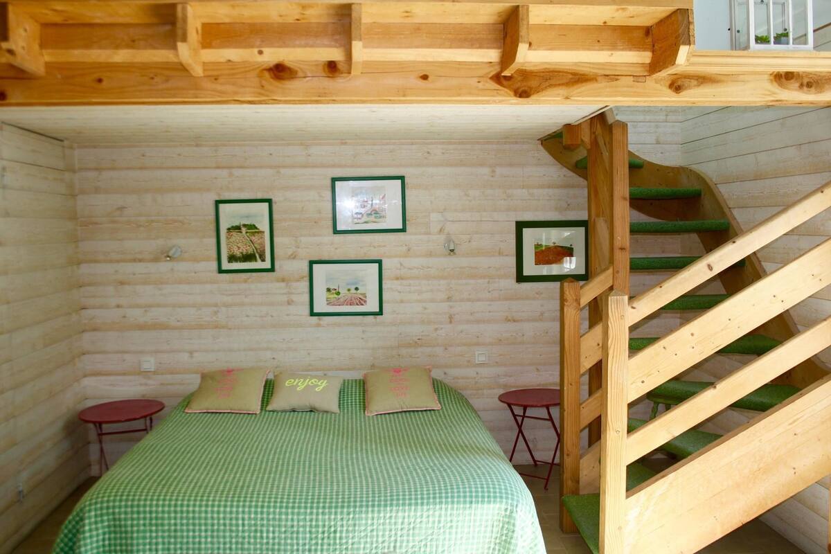 Un dormitorio rústico de madera con cama, una mesita, un sillón y una escalera de madera.