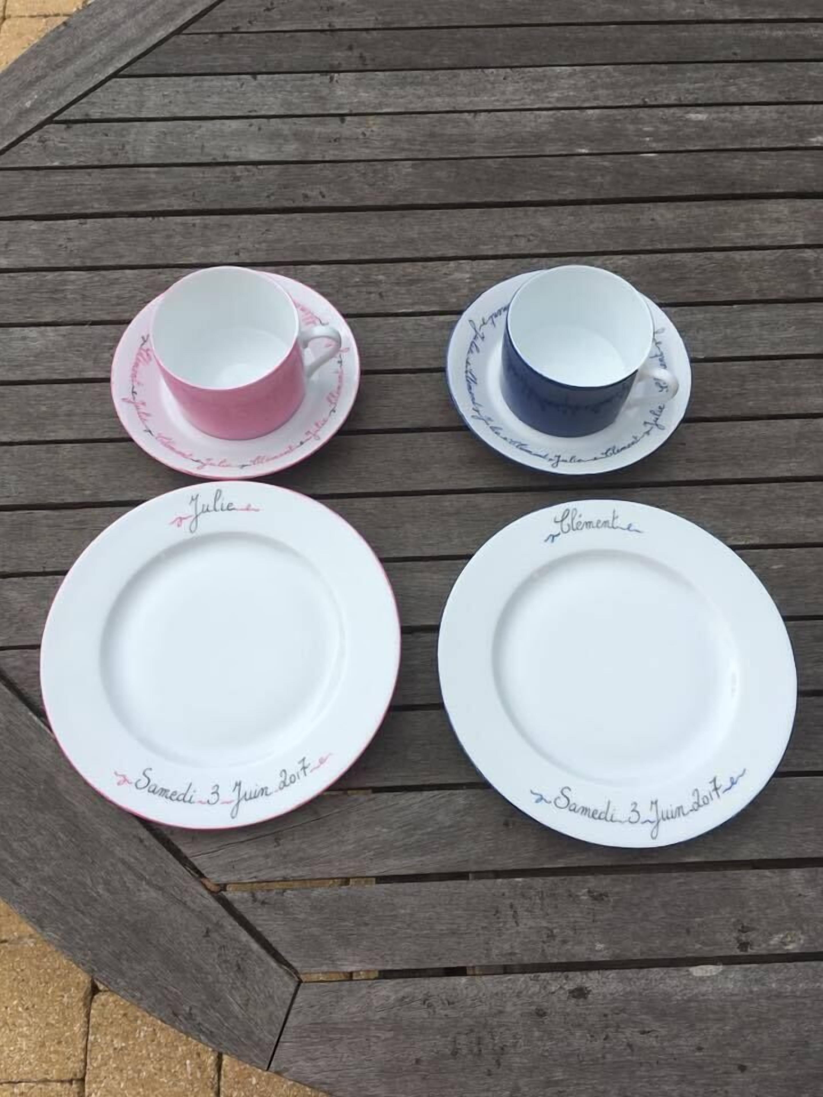 A wooden table with four white plates and two cups, each with handwritten text.