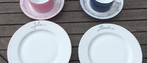 A wooden table with four white plates and two cups, each with handwritten text.