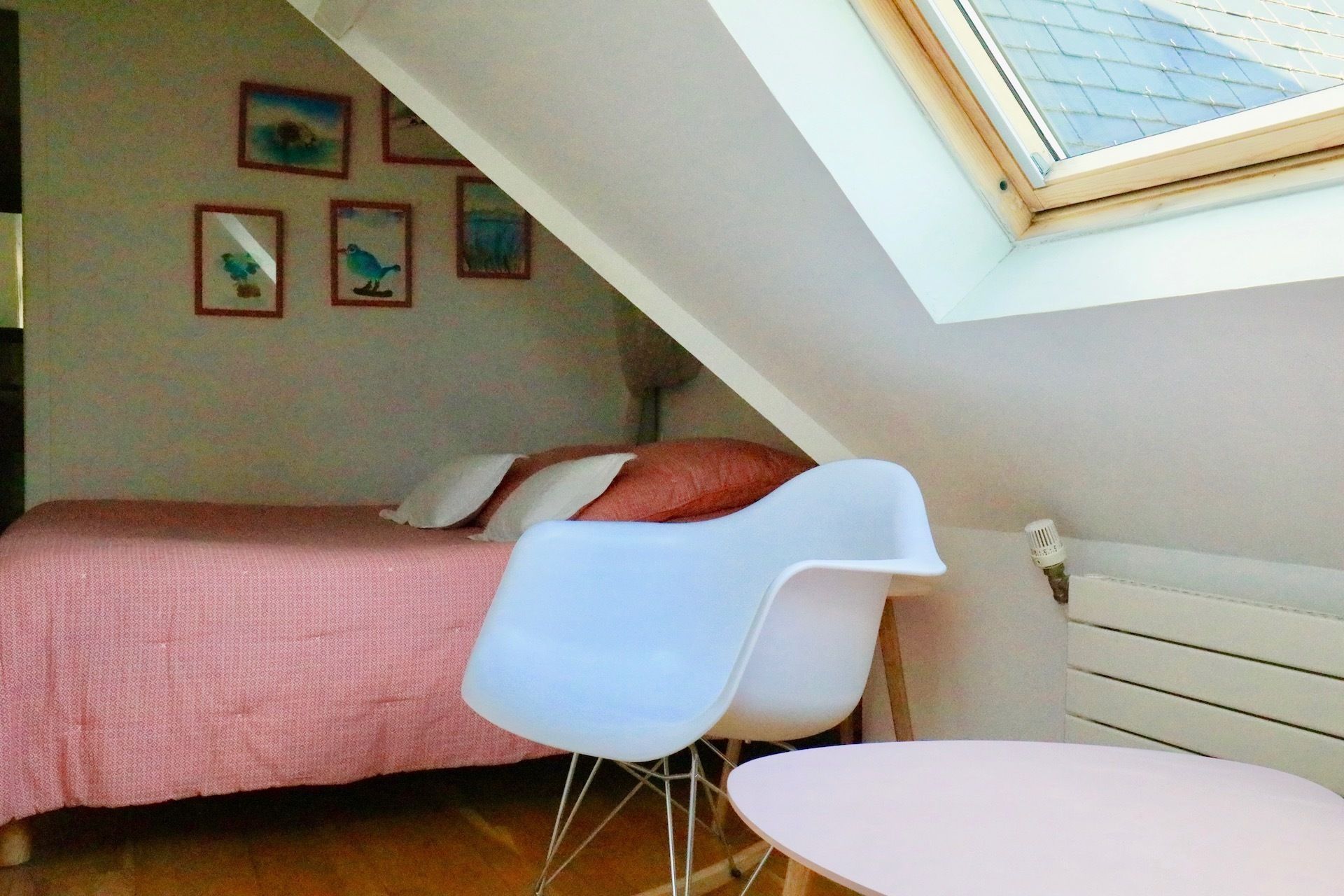 Ein kleiner, gemütlicher Raum mit einem Bett, einem weißen Stuhl, einem kleinen Tisch und einem Dachfenster.