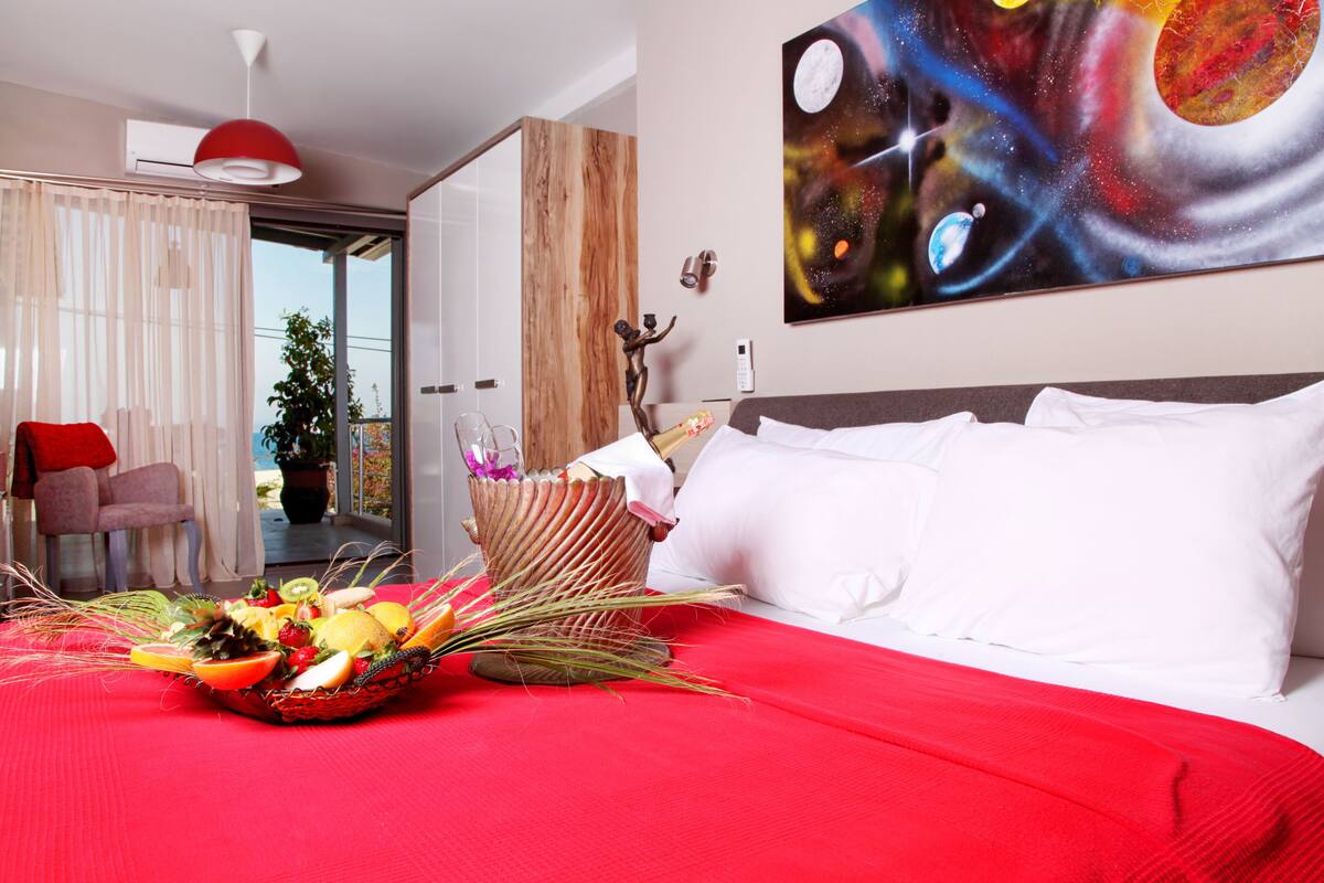 Ein Hotelzimmer mit einem großen Bett, einer Obstschale, einer roten Decke, einem Bild von Weltraum und Blick ins Freie.