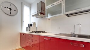A modern kitchen with red cabinets, a stainless steel sink, and a built-in stove. - Charming Castello Apartments by Wonderful Italy (Venice)