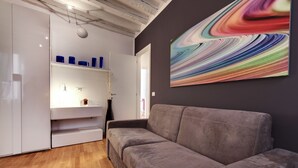 A modern living room with a sofa, a white cabinet with blue containers, and a colorful abstract painting on the wall. - Charming Castello Apartments by Wonderful Italy (Venice)
