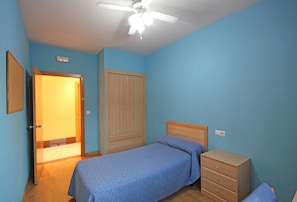 A bedroom with a single bed, a wooden wardrobe, a ceiling fan, and a door leading to another room. - Residencia Universitaria Cum Laude (Salamanca)