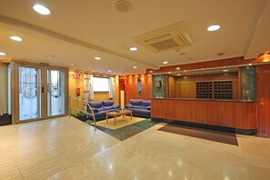 A hotel lobby with a reception desk, two sofas, a coffee table, and a glass door entrance labeled "SALIDA". - Residencia Universitaria Cum Laude (Salamanca)