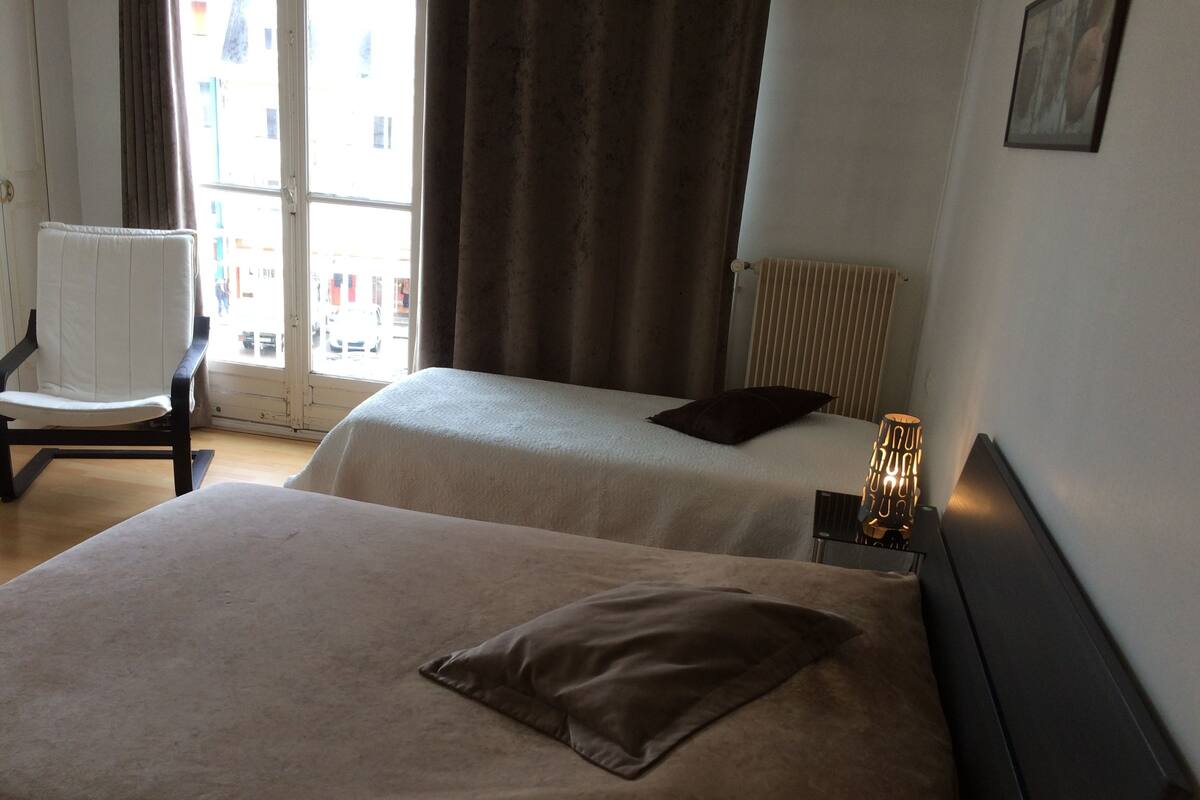 Une chambre d’hôtel avec deux lits, une chaise, un radiateur et une fenêtre avec des rideaux.