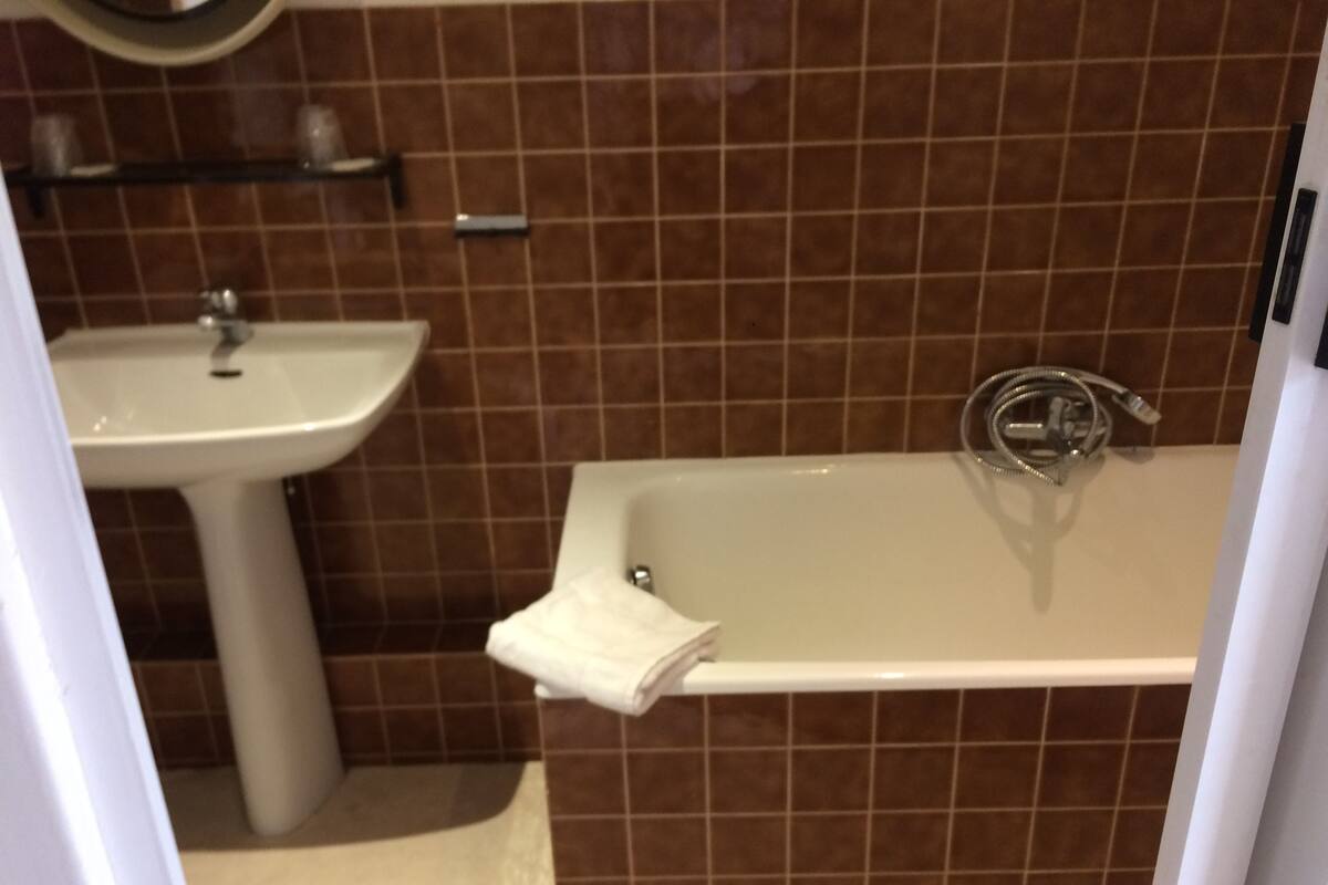Une salle de bain avec un lavabo, une baignoire et des murs recouverts de carreaux bruns.