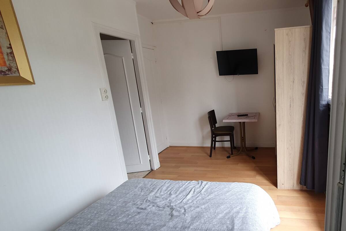 Une pièce comprenant un lit, un bureau, une chaise, un téléviseur et une porte.