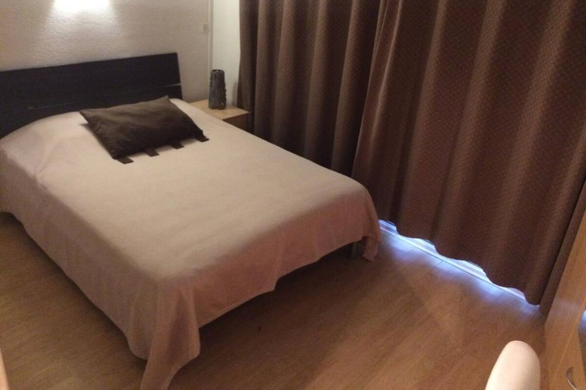 Un lit bien fait, avec un oreiller, une table de chevet avec une lampe et une fenêtre avec des rideaux.