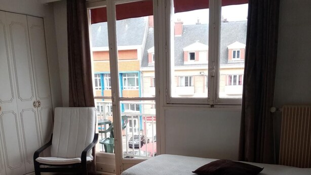 Habitación de hotel con dos camas, una silla y vistas a edificios a través del ventanal.