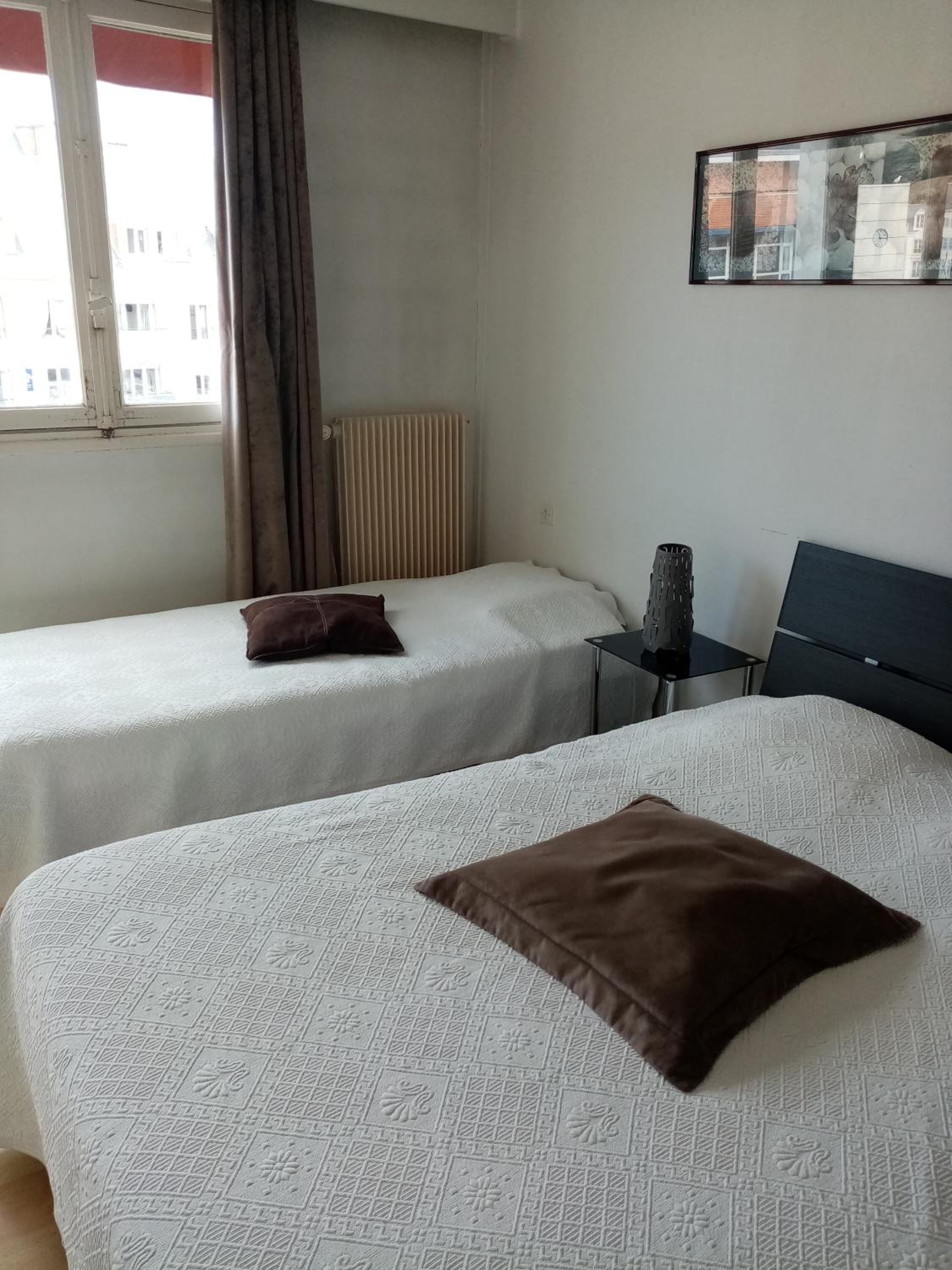 Une chambre d’hôtel avec deux lits, un radiateur, une petite table et un tableau encadré au mur.