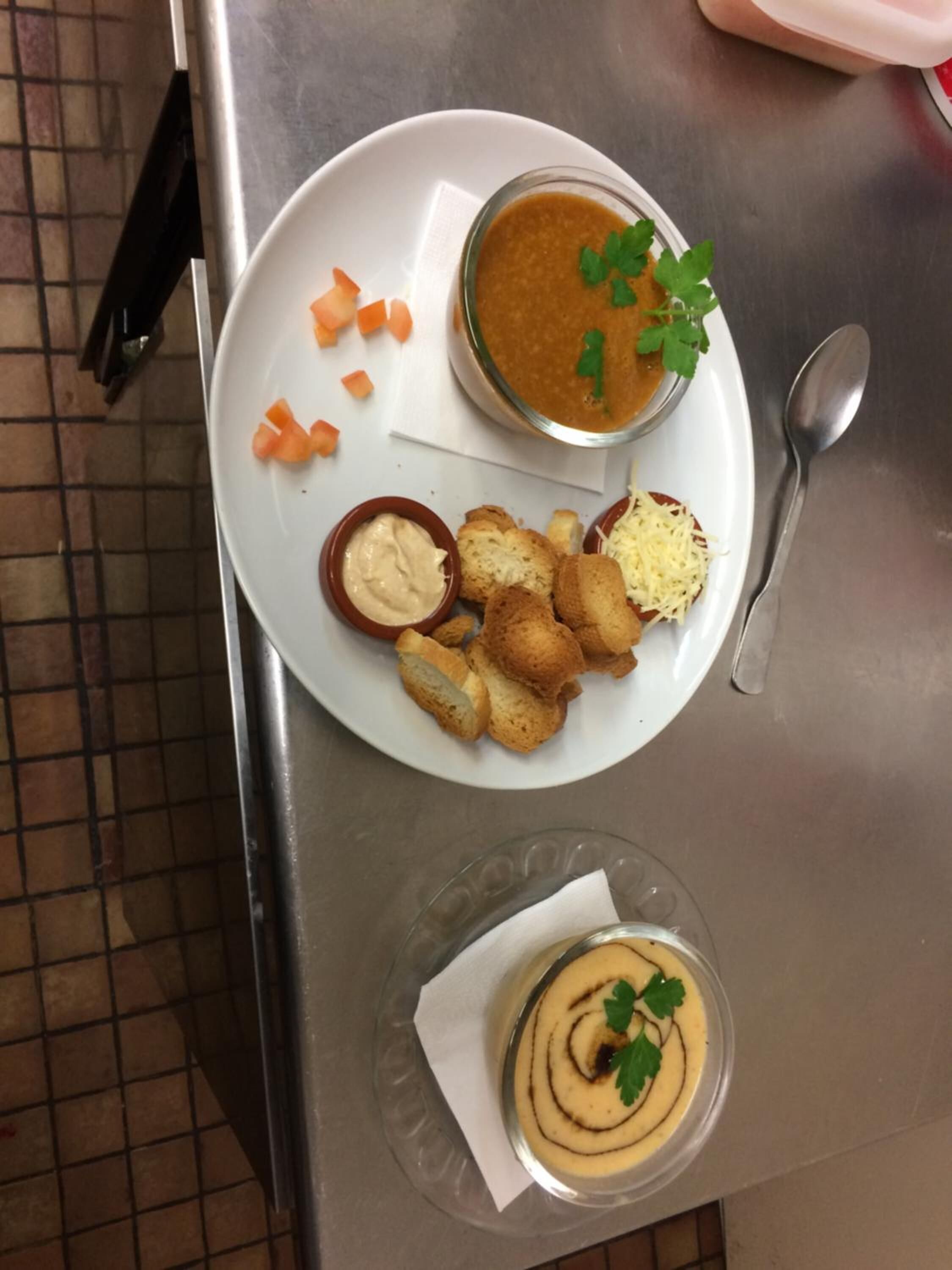 A plate with a bowl of soup, croutons, shredded cheese, and carrot sticks.