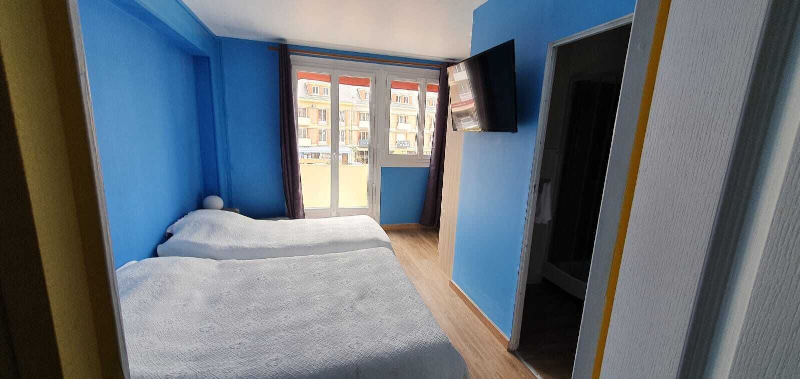 A room with two beds, a TV, and a view of buildings through a door.