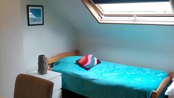 Une petite chambre avec un lit simple, une lucarne, une table de chevet, une chaise et un bureau.