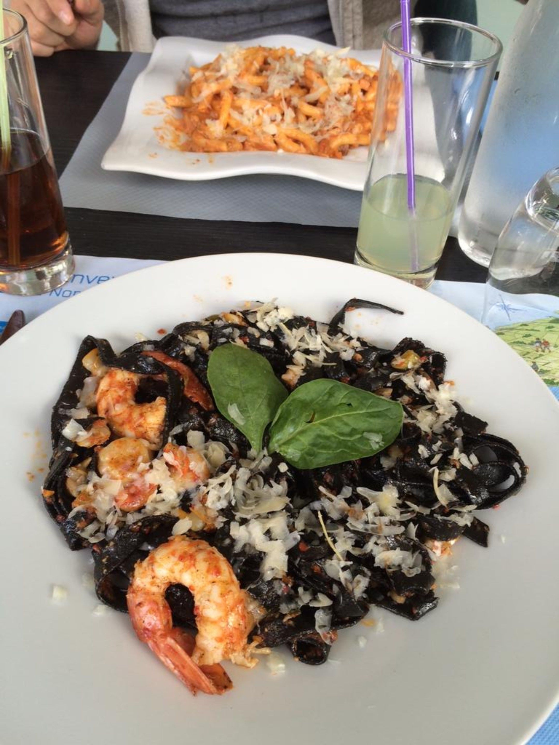 Un plato de pasta de mariscos con camarones y mejillones negros, decorado con hojas de albahaca.