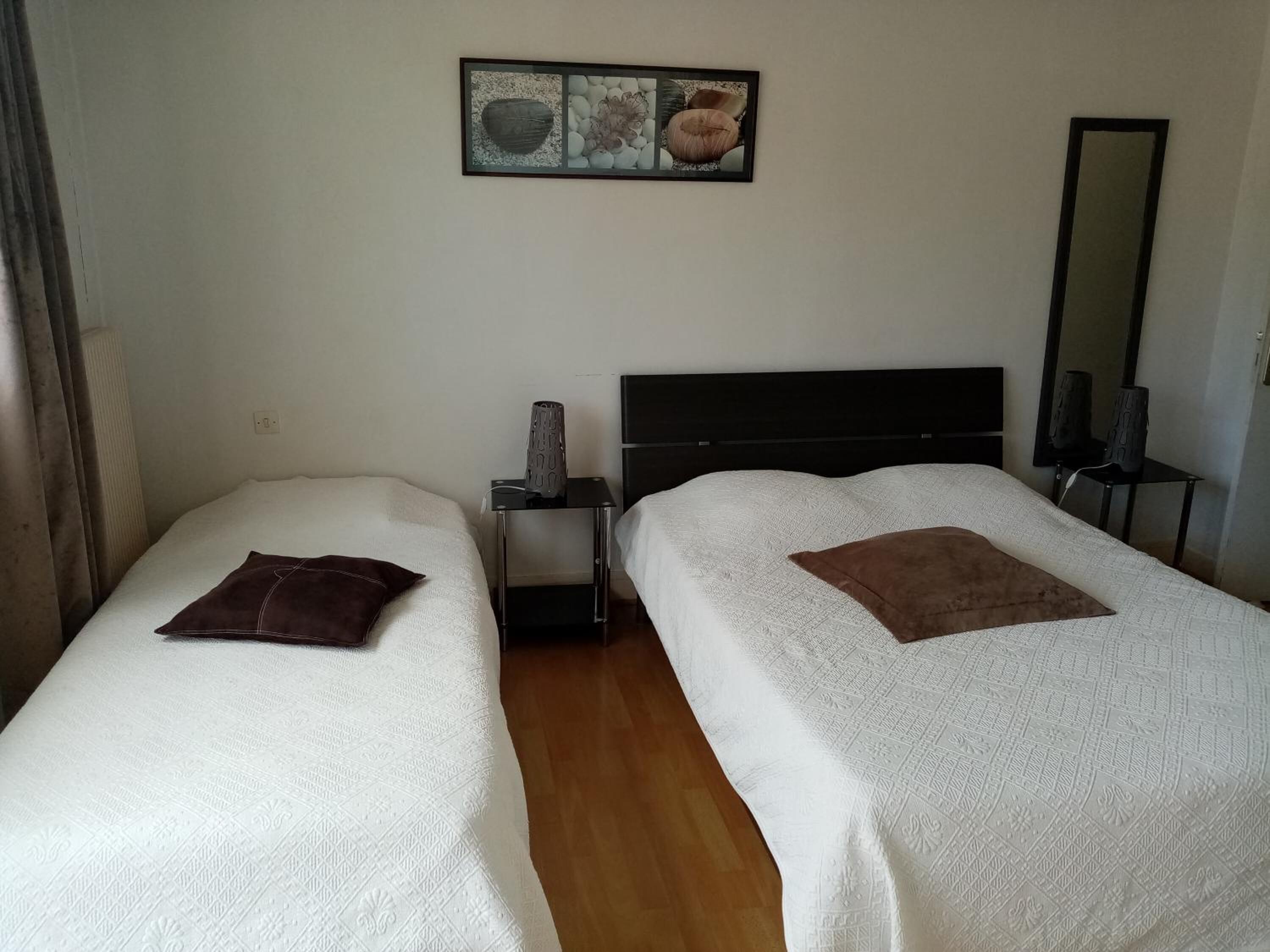 A double room with two beds, a nightstand, a lamp, a mirror, and a framed picture on the wall.