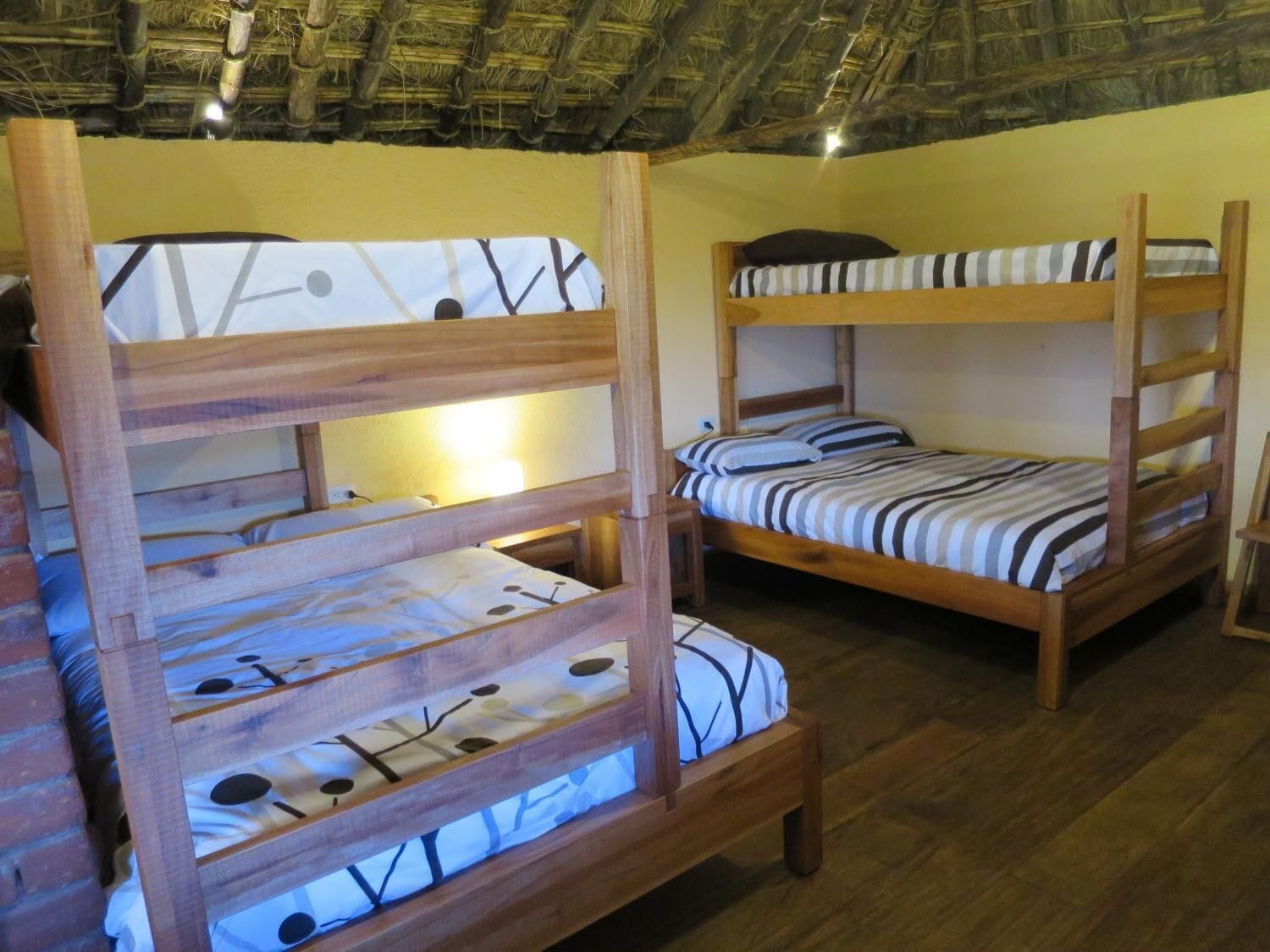 Una habitación con literas, cabeceros de madera y techo de paja.