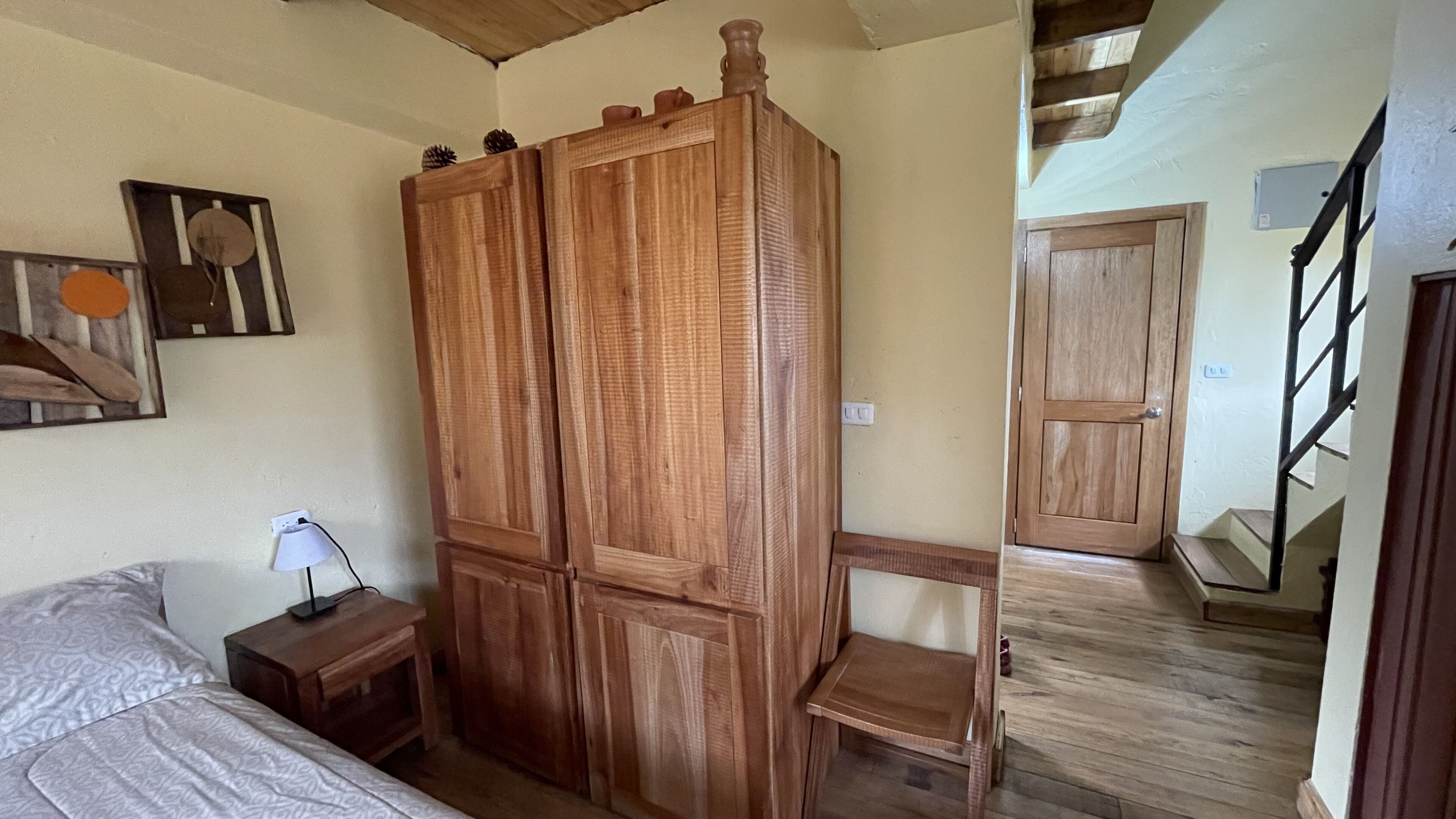 A bedroom with a bed, a wooden wardrobe, a nightstand, and a painting on the wall.