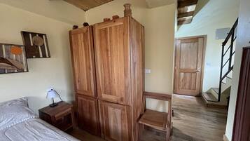 A bedroom with a bed, a wooden wardrobe, a nightstand, and a painting on the wall.