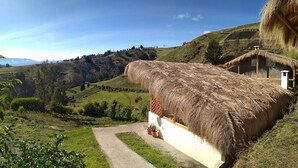 Una casa con techo de paja y fachada blanca, ubicada en un paisaje montañoso con cielo despejado.