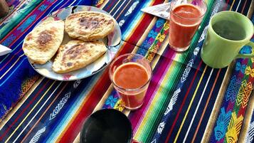 Un mantel tejido de colores con un plato de panes planos, dos vasos de bebida roja y una taza verde.