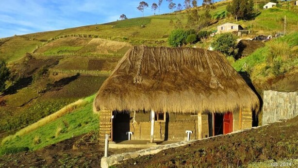 Una casa tradicional con techo de paja y base de piedra, ubicada en una colina bajo un cielo despejado.