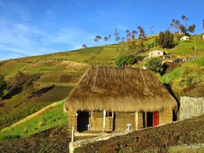 A traditional thatched-roof house with a stone foundation, set on a hillside with a clear sky. - Turismo Comunitario La Esperanza (Cajabamba)