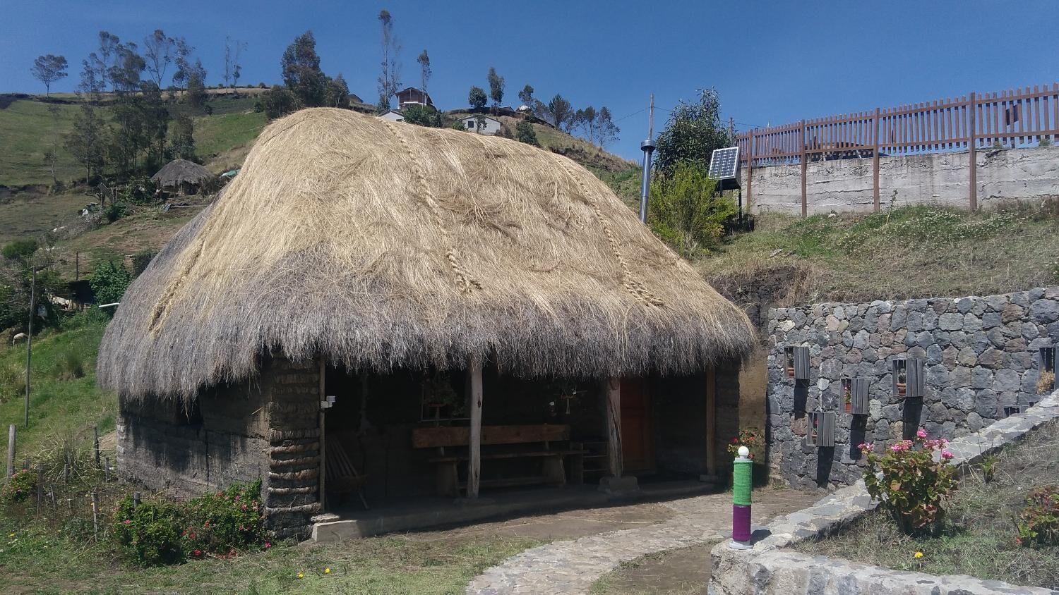 A rustic thatched-roof hut with a stone wall and a wooden bench outside.